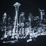 White graphic illustration of the Seattle skyline, featuring the Space Needle, on a dark fabric background—perfect for custom t shirts and printed tshirts. Rain City West