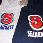 Two hoodies, one white and one navy, each displaying a large red "S" with a star and the word "SEAURST" printed below—perfect Seahurst Sweatshirts for showing school spirit at the WIAA Tournament. Rain City West
