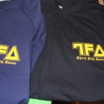 Two T-shirts, one navy blue and one black, feature the yellow "TFA" logo and "Thirty Fifth Avenue" text on the left chest, created with high-quality screen printing. Rain City West