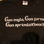 A black T-shirt with white screen printing text in Irish reading: "Gan eagla, Gan formad, Gan sprionlaitheacht”—perfect for showing your spirit on St. Patrick's Day. Rain City West