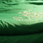 A stack of green T-shirts with a partially visible "St. Paddy's Day" screen printing design in white, perfect for celebrating St. Patrick's Day. Rain City West