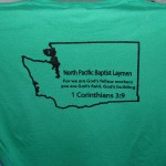 Green T-shirt with a black outline of Washington state, text about North Pacific Baptist Laymen, and a verse from 1 Corinthians 3:9. Perfect for those who love unique T-shirts and celebrating faith in style. Rain City West