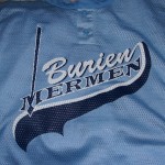 A light blue sports jersey with the words "Burien Mermen" in white and navy lettering across the front, perfect for pairing with matching hats or T-shirts. Rain City West