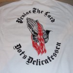 White t-shirt featuring praying hands with red lines and the text "Praise The Lord Nots Delicatessen" in black gothic lettering, inspired by the bold style of Praise the Lard t-shirts. Rain City West