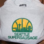 A gray t-shirt featuring a yellow and green graphic of the Seattle skyline and "SEATTLE SUPERSAUSAGE" below—perfect deli gear for fans of Dot's Deli. Rain City West