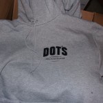 A gray hoodie with "DOT'S DELICATESSEN" printed in black on the chest lies on a cardboard box, showcasing classic Dot's Deli gear. Rain City West