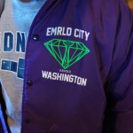 Person wearing a vintage "EMRLD CITY WASHINGTON" jacket with a green diamond graphic over a grey "IDN" shirt. Classic vintage jackets style for a standout look. Rain City West