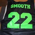 A black sports jersey with bright green screen printing, featuring the word "SMOOTH" and the number "22" on the back. Rain City West