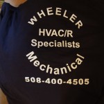 A navy t-shirt displays the text "WHEELER Mechanical HVAC/R Specialists 508-400-4505" in white letters, showcasing quality screen printing. Rain City West