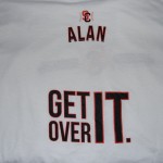 A white T-shirt with "ALAN" printed near the collar and "GET OVER IT." in large black letters on the lower back. Rain City West