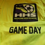 Two yellow sports shirts: the top features "HHS Highline High School Women's Soccer" with a soccer graphic, while the bottom boldly displays "GAME DAY." Perfect for school spirit and team pride. Rain City West