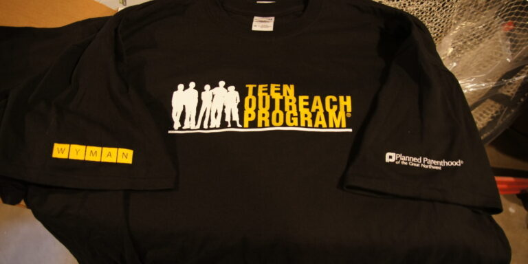 Black T-shirt featuring the "Teen Outreach Program" logo in yellow and white, with a Wyman logo on one sleeve and the Planned Parenthood logo on the other—perfect shirts for supporters of both organizations. Rain City West