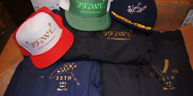 Various 35th Avenue Gear hats and jackets with logos and graphics are displayed on a table. Rain City West